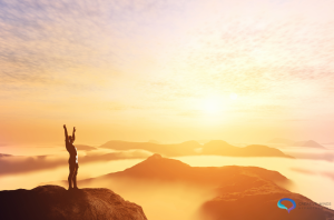 Person looking over the sunset and mountains achieving their dream